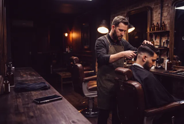 Barber Ozzy — a barber mid-fade in a moody barbershop, a phone resting on the counter