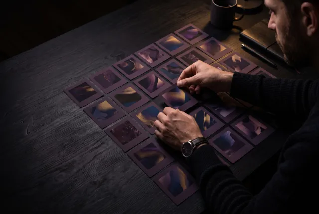 The Creative Pipeline — hands arranging a grid of printed ad mockups on a dark desk